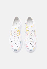 Λευκά παπούτσια τύπου low-top με πολύχρωμα αφηρημένα σχέδια, αστέρια, κορώνες, βέλη και καρδιές, σε συνδυασμό με λευκά κορδόνια σε ανοιχτό φόντο.