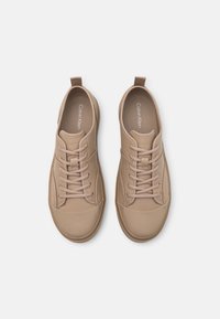 Para beżowych, niskich sneakersów Calvin Klein z sznurówkami, okrągłymi noskami i pętlami do zakupu, przedstawionych z góry na białym tle.