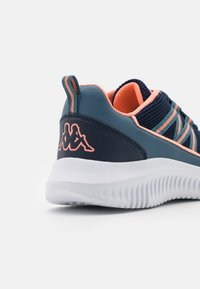 Marinblå träningsskor i mesh och syntetmaterial. Har rosa accenter, randiga snören och en vit texturerad sula. Utmärkande logotypdetalj.
