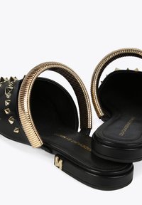Black slide sandals with metallic gold ring accents and silver studs. Flat soles with a glossy finish. Gold "M" detail on the side.