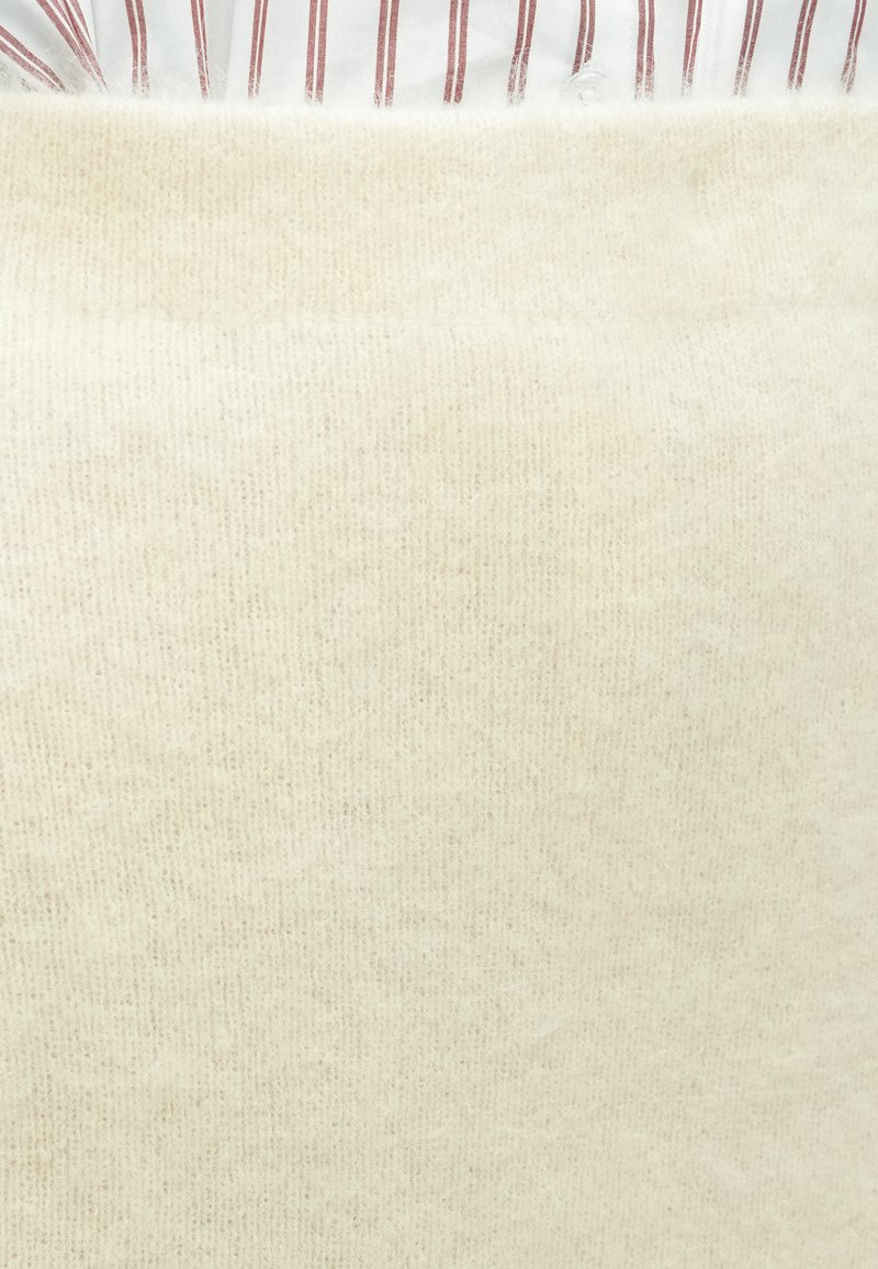 Person wearing a cream-colored fuzzy sweater over a white shirt with red vertical stripes, showing a close-up of the upper torso.