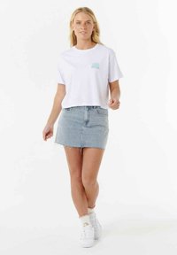 Weißes, gekürztes T-Shirt mit türkisfarbenem Sonnenlogo, kombiniert mit einem hellblauen Jeans-Minikleid und weißen Sneakers. Minimalistisches Design.
