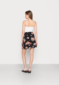 Saia floral preta com flores rosas e brancas, tecido leve, design em A, combinada com uma t-shirt branca e sandálias rasas.