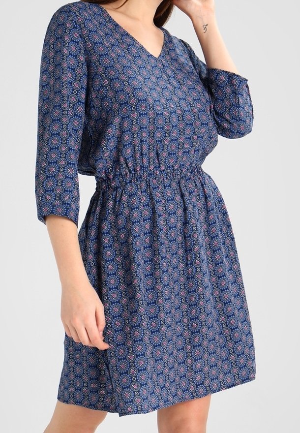 Robe bleue à motifs avec un décolleté en V, des manches trois quarts et une taille élastique. Le tissu présente un motif géométrique en rouge et blanc.