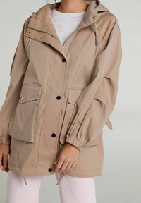 Beżowa, lekka kurtka z kapturem, zapinana na zamek, z dwiema przednimi kieszeniami, elastycznymi mankietami i sznurkiem ściągającym u dołu. Gładkie wykończenie materiału.