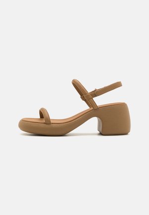 Beige sandal med åben tå, to tynde remme og en chunky mellemhøj hæl på hvid baggrund.