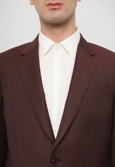 Blazer bordeaux en tissu texturé, avec un revers cranté, fermeture à un bouton et une poche poitrine, associé à une chemise blanche.