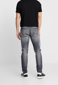 Vaqueros skinny gris deslavado con un diseño clásico de cinco bolsillos, ligero desgaste y un sutil aclarado en las costuras, combinados con zapatos negros.
