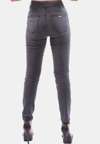 Jeans gris de cintura alta, ajustados al cuerpo, con una textura suave, diseño de cinco bolsillos y detalles de costura mínimos. Llevados con tacones altos negros.