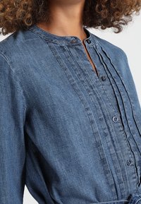 Jeansskjorta med knappstängning, subtil plissering fram, rundad krage och textil i mörkblå färg.