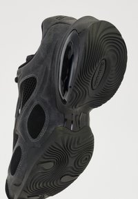 Chaussures de sport noires avec un mélange de matériaux texturés, des panneaux en maille et un design supérieur unique avec de grandes découpes. Semelle en caoutchouc épaisse.