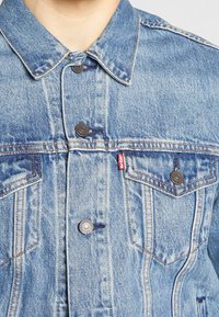 Chaqueta de denim azul claro con cuello puntiagudo, dos bolsillos en el pecho, botones plateados y etiqueta roja con el logo de Levi's en el bolsillo izquierdo.