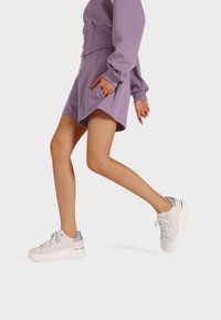 Sneakers in materiale sintetico bianco con una suola spessa, dettagli argentati sul tallone e una parte anteriore con lacci testurizzati.