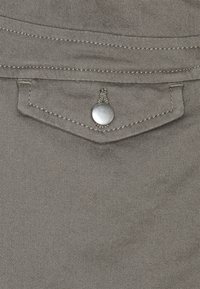 Szara, teksturowana tkanina z ozdobnym guzikiem i detalem szwu. Posiada małą, skośną kieszonkę nad główną częścią.