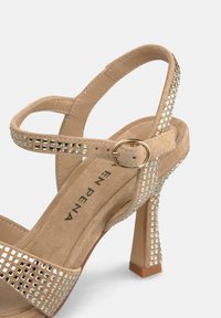 Beżowe sandały na wysokim obcasie z licznymi paskami, ozdobione błyszczącymi cyrkoniami, z teksturowaną zamszową wkładką i słupkowym obcasem.