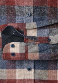 Koszula flanelowa zapinana na guziki w czerwono-niebiesko-beżową kratę. Posiada ciemne guziki, kontrastującą wewnętrzną mankietkę oraz teksturowaną tkaninę.