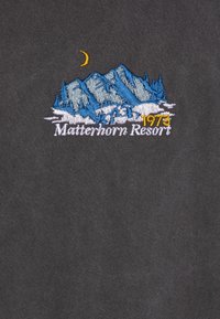 Černá látka s vyšitým vzorem hor v modré a bílé barvě, se žlutým měsícem a textem "Matterhorn Resort 1973" pod ním.