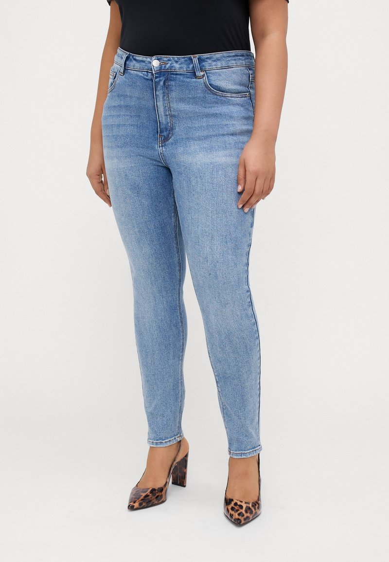 Vaaleansiniset kapeat farkut, joissa on viisi taskua, nappi ja vetoketjulaclosure, yhdistetty mustan paidan ja leopardikuvioisten korkokenkien kanssa. Sileä farkkukangas.