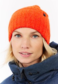 Heldere oranje gebreide beanie met een geribbeld patroon en een opgerolde rand. Heeft een klein zwart merketiket aan de zijkant.