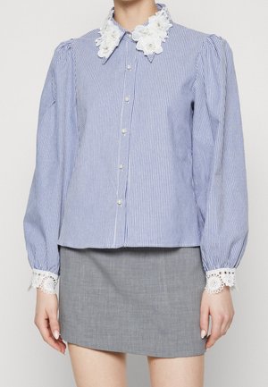 Sinivalkoraidallinen pusero, jossa on puhvimaiset pitkät hihat, kukkakuvioinen pitsikaulus ja kalvosimet, yhdistetty harmaaseen minihameeseen.