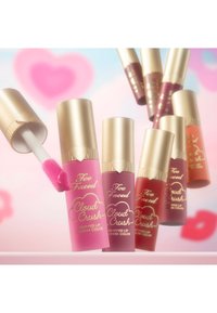 Eight tubes of Too Faced Cloud Crush Whipped Lip and Cheek Color with gold caps, displaying various shades of pink, red, and coral.
