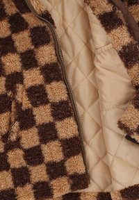 Bruin en tan geruit fleecjasje met een rits aan de voorkant en gewatteerde beige voering, met een zachte textuur en stiksel details.