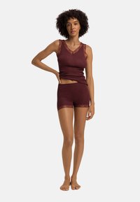 Burgundin neuletoppi, jossa on V-pääntie ja pitsireunus kaula-aukossa ja käsivarsissa, yhdistettynä vastavärisiin shortseihin, joissa on pitsikoristelu helmassa.