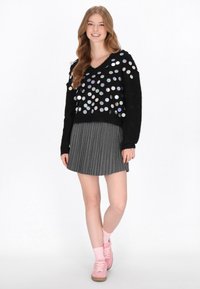 Czarny sweter z srebrnymi, okrągłymi cekinami, w połączeniu z szarym, plisowanym spódnicą i różowymi sneakersami w dopasowanych skarpetkach.