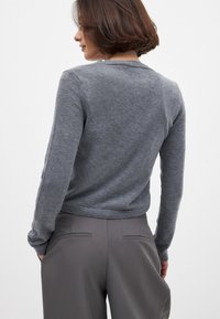 Gray knitted sweater with long sleeves, rounded neckline, ribbed cuffs, and hem. The back view shows a smooth texture, paired with gray trousers.