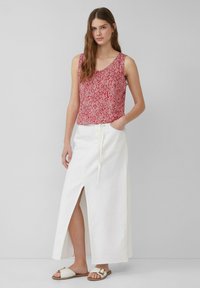 Top senza maniche a fantasia rossa, gonna maxi bianca con spacco frontale e sandali leggeri. Tessuto testurizzato e design semplice.