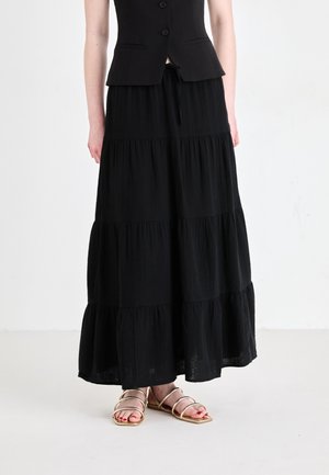 Gonna lunga nera a balze con una vestibilità morbida, presenta orli arricciati e una cintura elastica, abbinata a sandali metallici con cinturini.