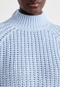 Ανοιχτό μπλε πλεκτό πουλόβερ με ψηλό ριχτό γιακά, υφασμάτινο μοτίβο με κάθετες ραφές και χαλαρή εφαρμογή.
