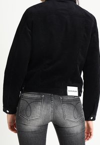 Černá kordurová bunda s límcem, zapínáním na knoflíky a štítkem. Vybledlé černé džíny se dekorativním prošíváním na zadních kapsách.