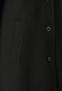 Abrigo de lana negra con textura suave, seis botones negros y un bolsillo lateral oculto para un diseño limpio.