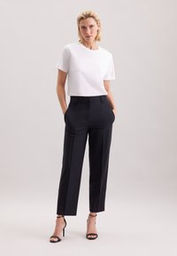 Witte T-shirt met korte mouwen gecombineerd met marineblauwe, hooggetailleerde, op maat gemaakte broek. Draagt zwarte sandalen met dunne bandjes en hoge hakken. Gladde stoftextuur.