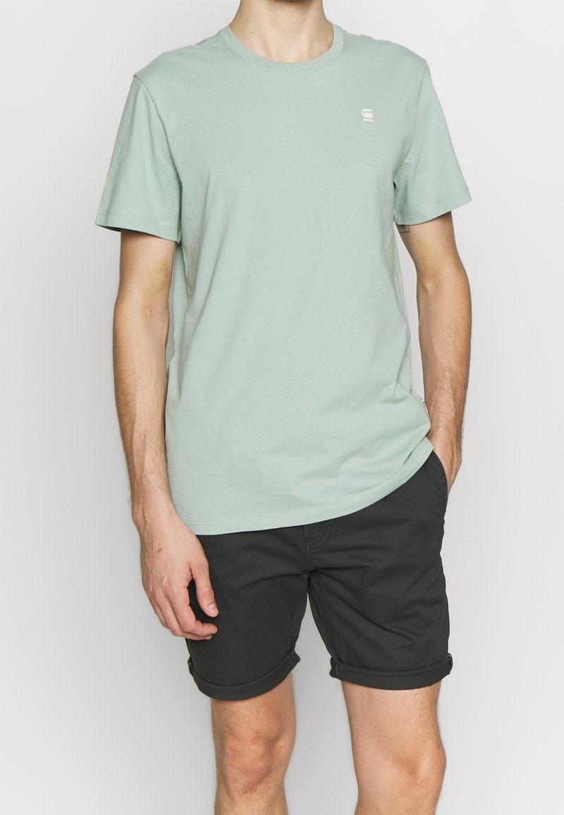 T-shirt di cotone verde chiaro con scollo a girocollo e maniche corte, abbinato a pantaloni corti neri arrotolati. Semplice logo sul petto.