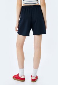 Pantaloni corti neri realizzati in un tessuto morbido con una cintura elastica. Il design è semplice e dritto, raggiungendo metà coscia.