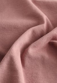 Mjuk rosa tyg med en jämn textur och finstickad konstruktion. Materialet faller mjukt och visar på milda vågor och veck.