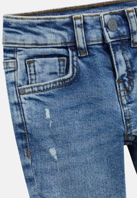Bleka blå denimjeans med slitna detaljer, femfickorsdesign, kontrasterande beige sömmar och en knappstängning vid midjan.