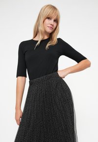 Svart tettsittende topp med trekvartslange ermer, kombinert med en lang, svevende svart tyllskjørt med et subtilt leopardmønster.