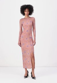 Long-sleeved, slim-fit dress in peach fabric with a light abstract pattern, featuring a side slit and flat seams, paired with black heels.