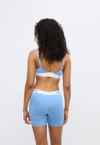 Μπλε βαμβακερό σουτιέν και ταιριαστά μποξεράκια με λευκές λάστιχες με λογότυπο. Λεπτή υφή, ρυθμιζόμενες τιράντες και απλός σχεδιασμός. Εμφανίζεται η πίσω όψη.