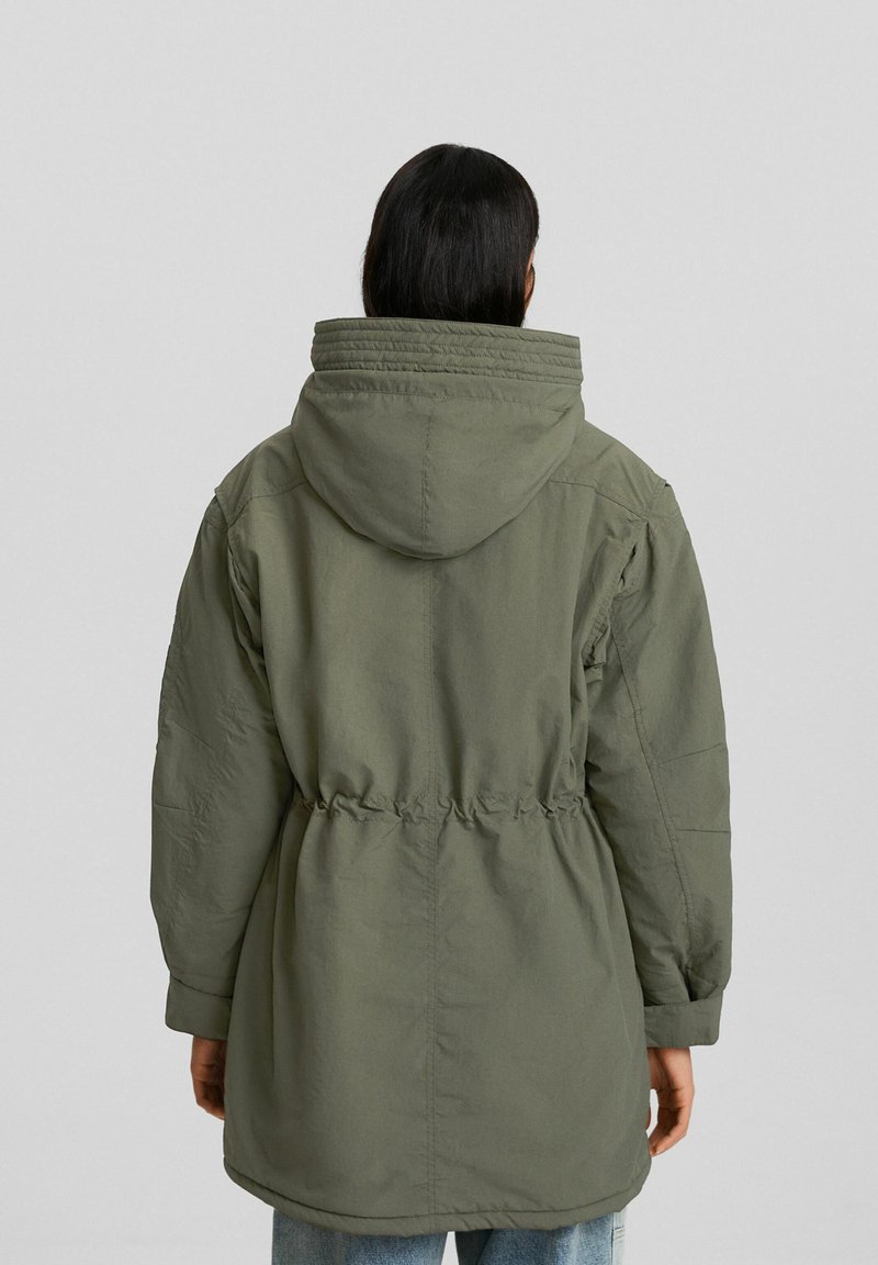 Parka olive avec une capuche, taille à cordon et manches longues. Le tissu a une texture douce et une coupe décontractée.