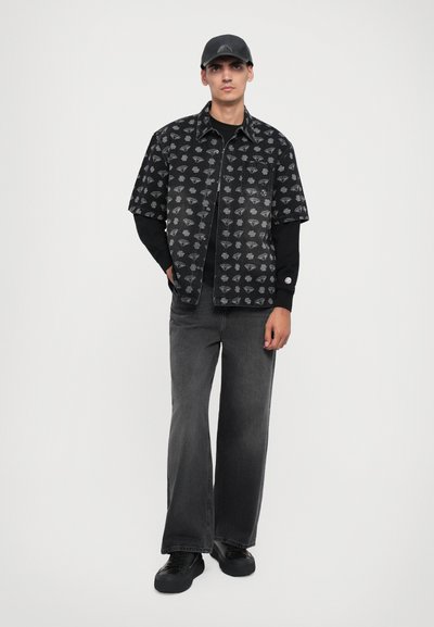 Short-sleeve black shirt with diamond pattern, paired with a black long-sleeve top, gray wide-leg jeans, and black sneakers. Black cap included.