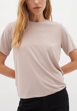 T-shirt a maniche corte di colore rosa chiaro, realizzato in tessuto morbido, con colletto rotondo e drappeggio discreto, abbinato a pantaloni neri.