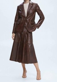 Ruskea nahkatakki ja laskostettu hamekokonaisuus, teksturoitu pinta, räätälöity muotoilu, takissa taskut ja hameessa liehuva siluetti.