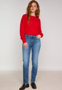 Maglione rosso a maniche lunghe abbinato a jeans attillati azzurri. I jeans presentano un classico design a cinque tasche e una texture leggermente sbiadita.