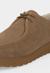 Κοντινό πλάνο καφέ καστόρινο casual παπούτσι με ραφή moc-toe, δύο οπές για κορδόνια και υφασμένο λαστιχένιο πέλμα.