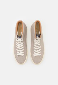Høye sneakers i lys beige semsket skinn med hvite lisser, tan lærkrage og grå detaljer. Rund tå og gummisåle.