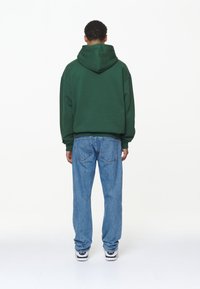 Vihreä huppari, jossa on huppu, löysä malli ja elastiset hihansuut; yhdistetty vaaleansinisiin, rentoihin farkkuihin, joissa on takataskut.